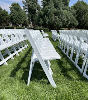Rows of sleek black folding chairs lined up for a formal ceremony in a garden.