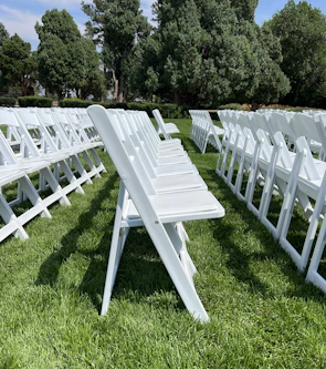 A spacious green lawn with white chairs arranged for an outdoor social gathering under a clear blue sky.