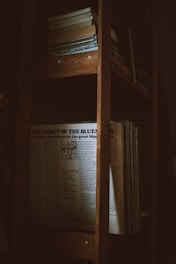A dimly lit wooden bookshelf contains several books and a prominently displayed album cover or record titled 'The Legacy of the Blues'. The light softly illuminates the text, creating a serene and nostalgic atmosphere.