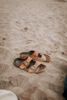 Close-up of brown leather sandals resting on a sandy beach with soft sunlight.