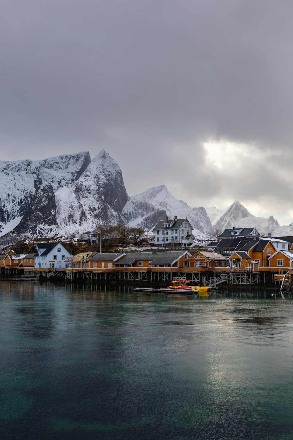 a group of houses by a body of water with mountains in the background with Lofoten in the background