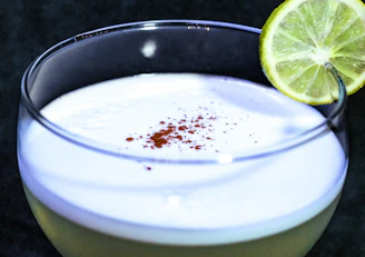 Fresh pisco sour cocktail with a frothy top and a slice of lime on a sleek bar counter.