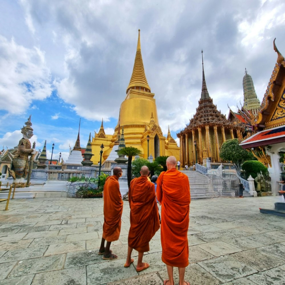 a group of men in orange robes with Wat Phra Kaew in the background