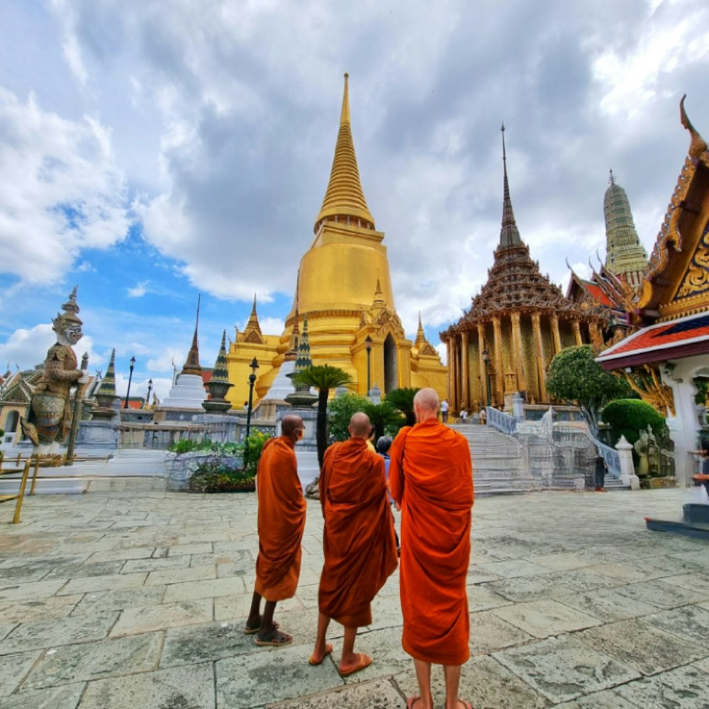 un grupo de hombres con túnicas naranjas con Wat Phra Kaew en el fondo