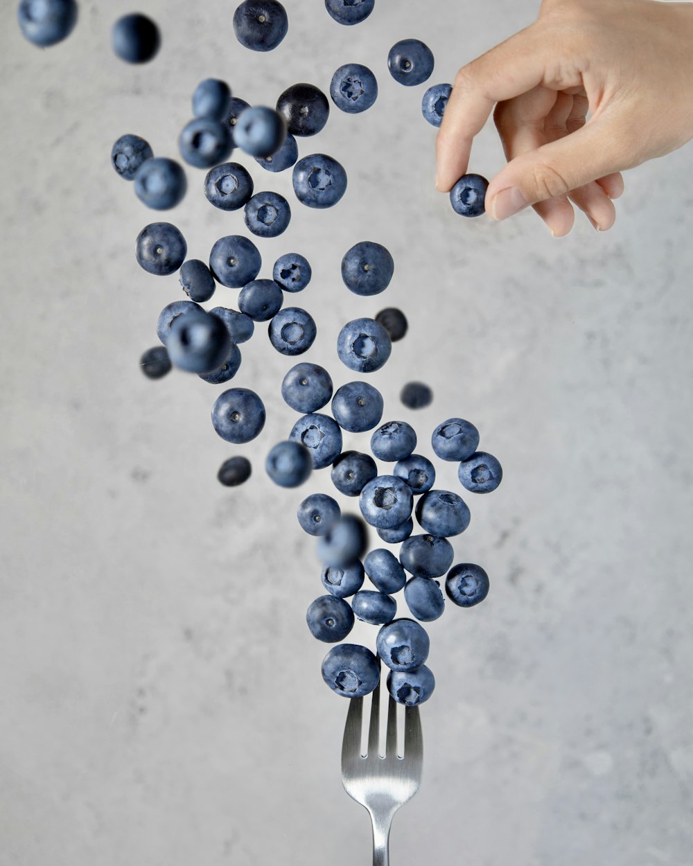 a hand holding a fork over a pile of blueberries