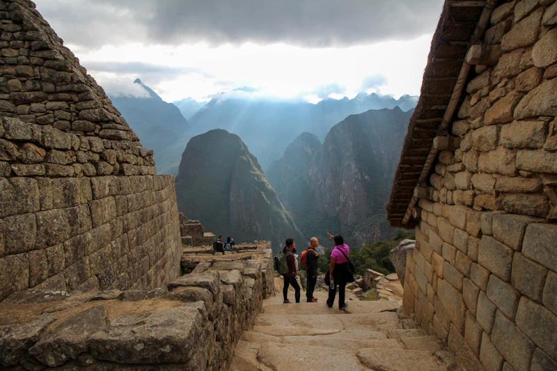 Visitors walking a stone path between Inca walls at Machu Picchu with mist over the mountains