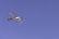 A light aircraft with a propeller is flying at a significant altitude against a clear blue sky. The plane has a sleek design and the registration number 'N323KG' is visible on its body.