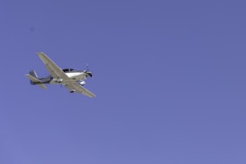 A light aircraft with a propeller is flying at a significant altitude against a clear blue sky. The plane has a sleek design and the registration number 'N323KG' is visible on its body.