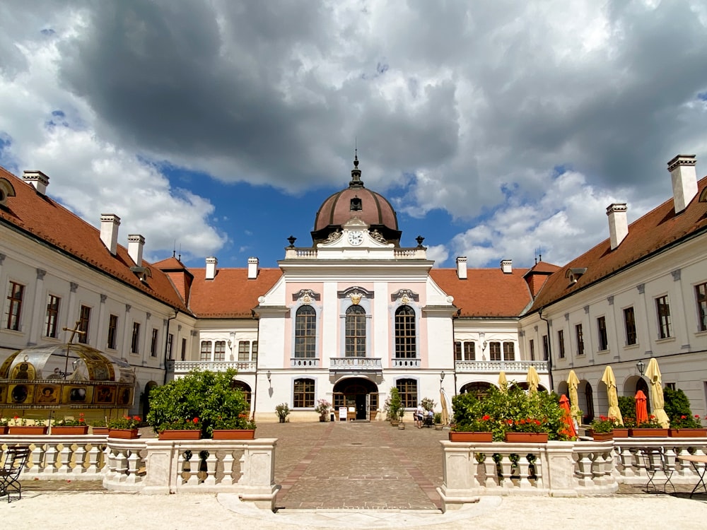 a large white building with a domed roof and a courtyard with tables and chairs and a cloudy sky