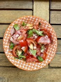 Fresh tomato salad drizzled with Redburst Ketchup, garnished with basil leaves on a rustic wooden table.