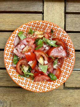 A vibrant bowl of fresh colorful salad with greens, tomatoes, and nuts on a wooden table.