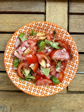 A colorful bowl of fresh salad with vibrant red tomatoes and greens on a rustic wooden table.