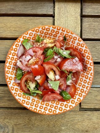 Fresh tomato salad drizzled with Redburst Ketchup, garnished with basil leaves on a rustic wooden table.
