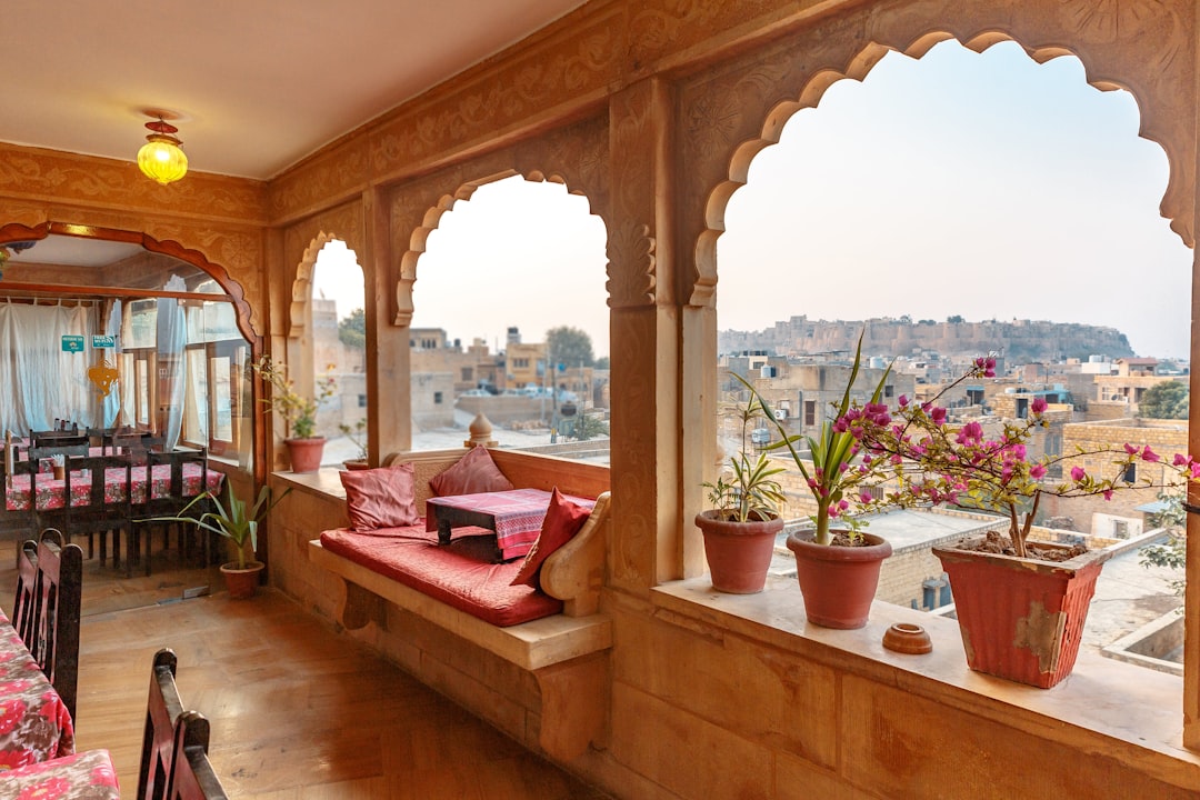 a room with a large window and a couch and potted plants, Lal Garh Fort And Palace - Set in an ornate building, this elegant hotel is a kilometre from the iconic 12th-century Jaisalmer Fort, 1.5 km from the Desert Cultural Centre and 1.6 km from the Folklore Museum.<p></figure>Featuring carved stonework and traditional Rajasthani decor, the colourful rooms & suites offer free Wi-Fi, satellite TV and air-conditioning; some have balconies. Room service is 24/7.</p><p>Amenities include a relaxed restaurant with a covered rooftop dining area, which serves both regional and international cuisine. The hotel also organises desert safari. It is opertional for 24hours.
