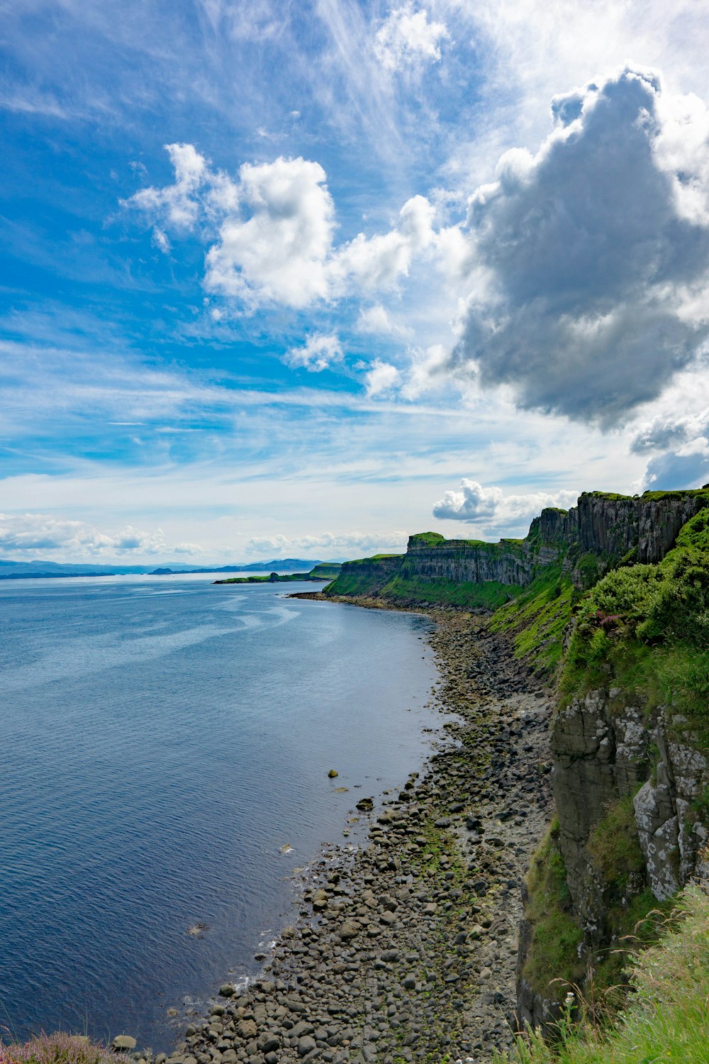 a rocky beach with a body of water and a hill with a hill with a blue sky and