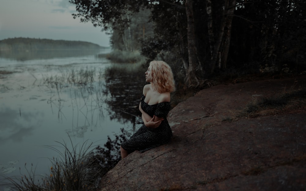 a person sitting on a rock by a lake