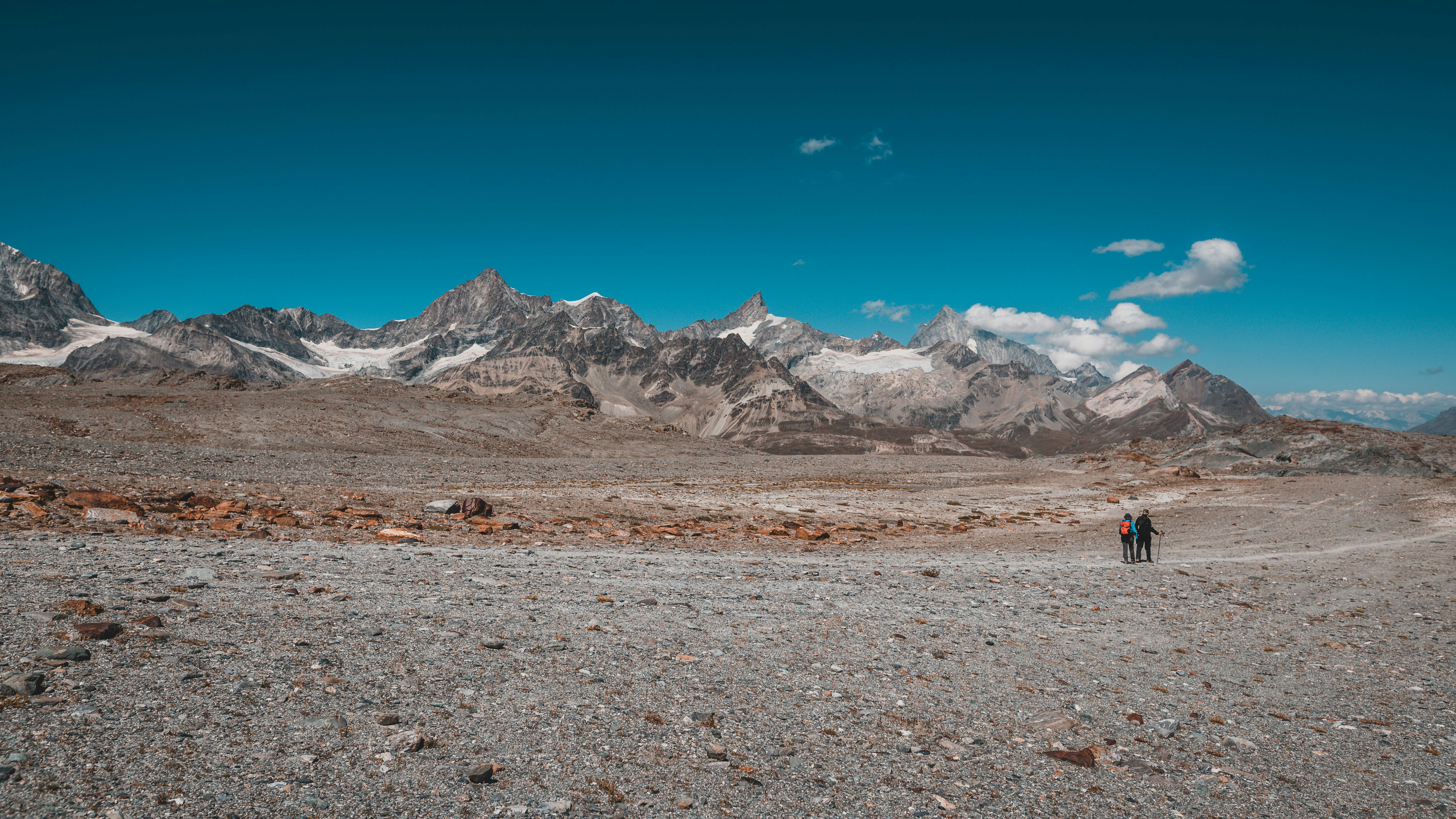 a couple people walking on a rocky terrain with mountains in the background