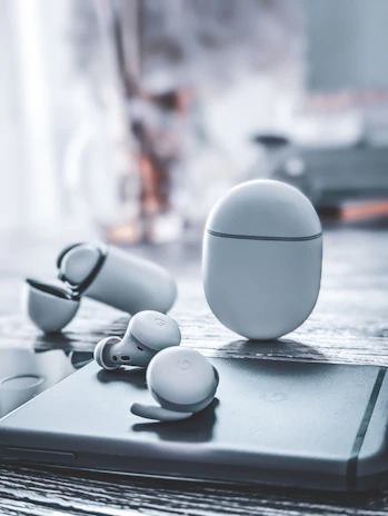 A pair of wireless earbuds in their charging case, set on a smooth marble surface with subtle shadows.