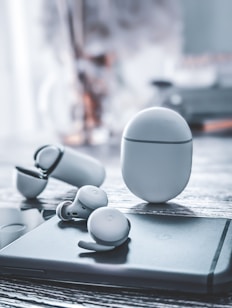 A pair of wireless earbuds and their charging case are placed on a sleek, modern surface. The design is minimalistic with a smooth, rounded shape. The backdrop is blurred, creating a focus on the earbuds.