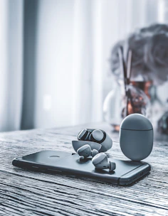 A pair of wireless earbuds next to a smartphone playing a soothing audiobook, set on a wooden table.