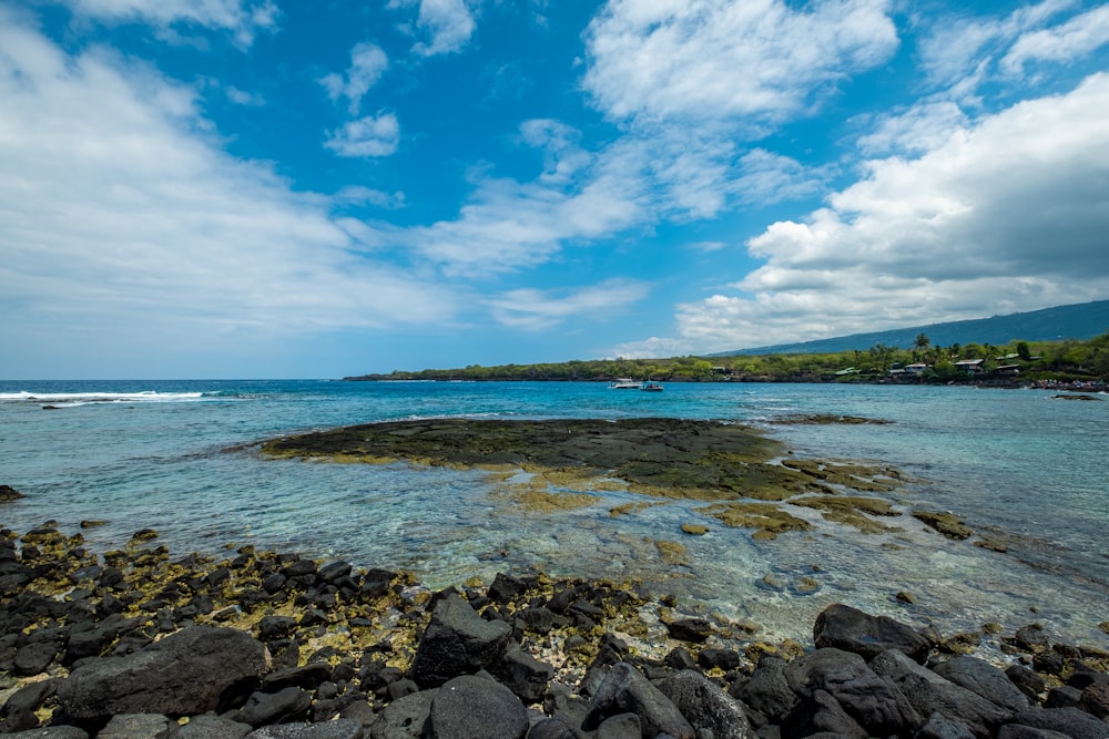 a rocky beach with a body of water and hills in the background