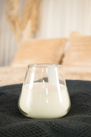 Close-up of a linen pillow on a comfy chair beside a neat utility cart holding a glowing glass candle stand.