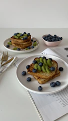 Lifestyle shot of a morning breakfast table featuring toast with honey and fresh fruit, bathed in soft natural light.