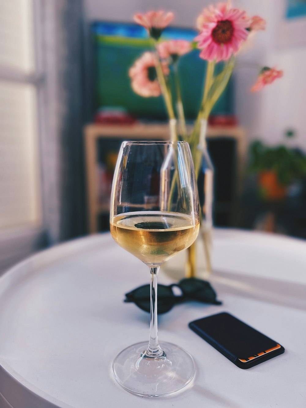 a glass of wine next to a cell phone and a vase of flowers