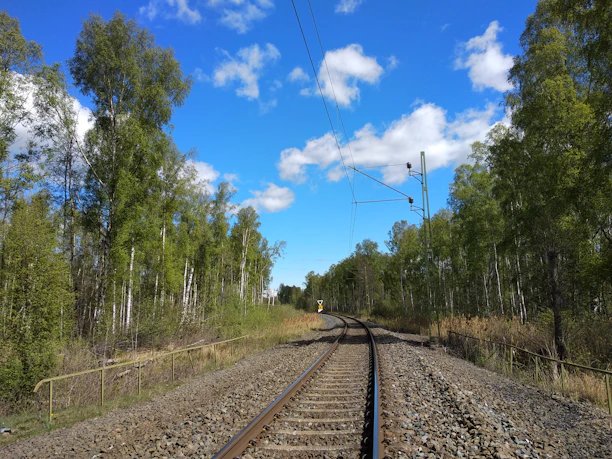 A construction crew working on a railway track surrounded by lush greenery under a clear sky.