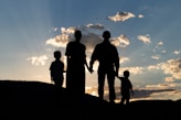 a group of people standing on a hill looking at the sunset