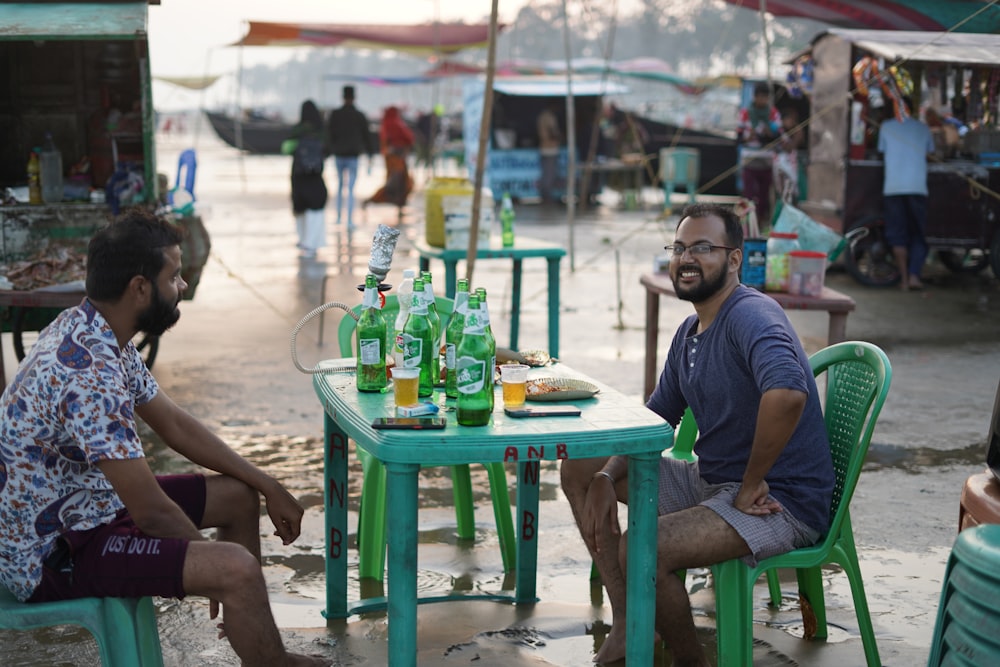 a couple of men sitting at a table with food and drinks