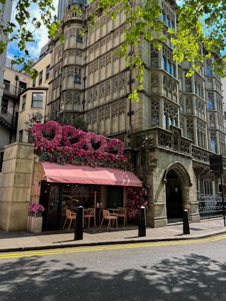 An inviting café storefront adorned with pink accents and lush greenery on a sunny day.