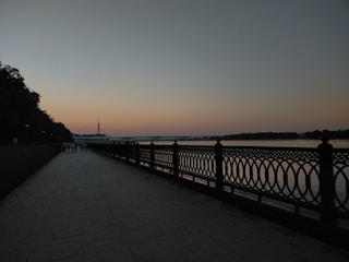 Residents enjoying a walk along a tree-lined riverside promenade during sunset.