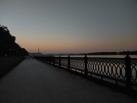 Residents enjoying a walk along a tree-lined riverside promenade during sunset.