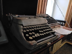 A vintage typewriter on a wooden desk surrounded by tools and papers.