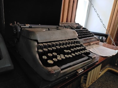 A vintage typewriter on a wooden desk surrounded by tools and papers.