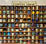 Colorful hand-painted ceramic mugs lined up on a wooden shelf with island views.