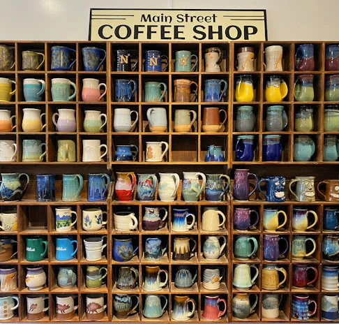 A variety of printed mugs with unique logos and artwork displayed on shelves.