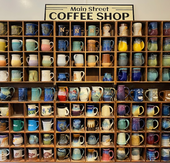 A collection of colorful, artistic mugs displayed on a wooden shelf.