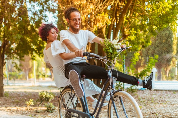Couple laughing together while riding bicycles through a park.