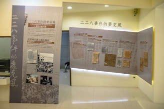 A museum exhibit features large panels with images and text related to the 228 Incident, displayed in a well-lit, modern room. One panel includes news clippings and historical photographs, while the other displays documents. The exhibit is presented in both Chinese and English.