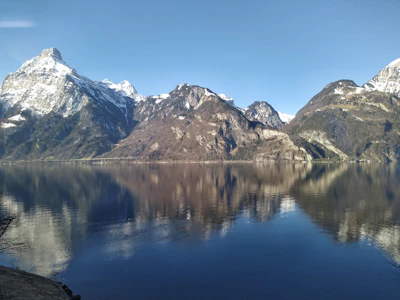 A serene thumbnail of snow-capped mountains reflecting in a crystal-clear lake in Switzerland.