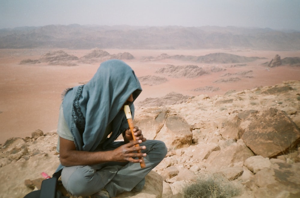 a man sitting on a rock with a gun in his hand