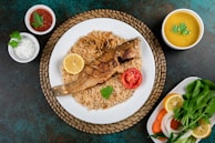 Grilled fish served on a rustic wooden board with lime wedges and a side of rice.