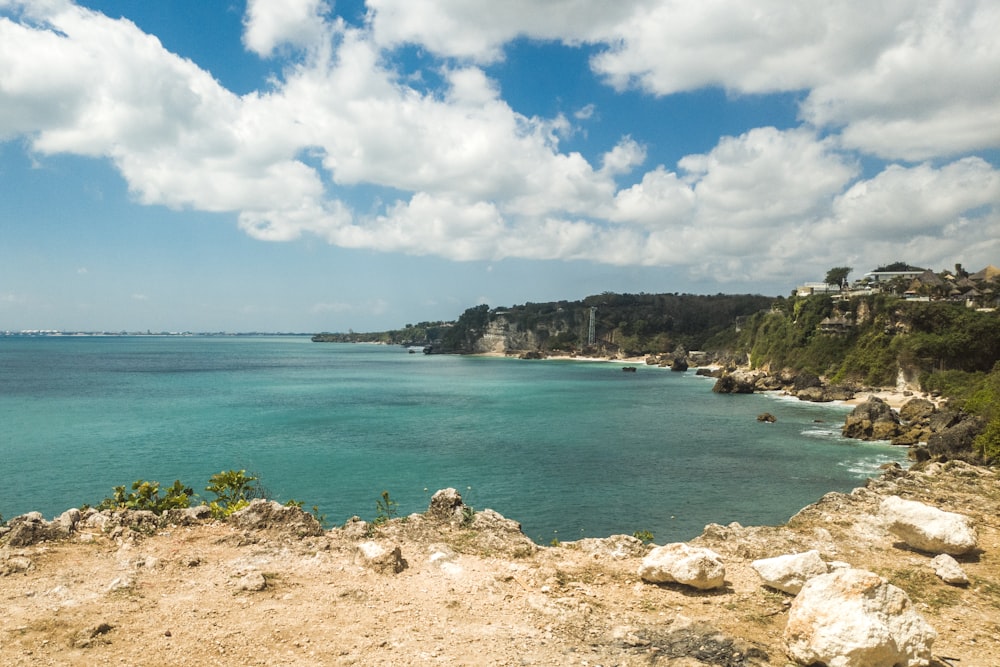 a rocky beach with a body of water and a land with a hill with a building on it