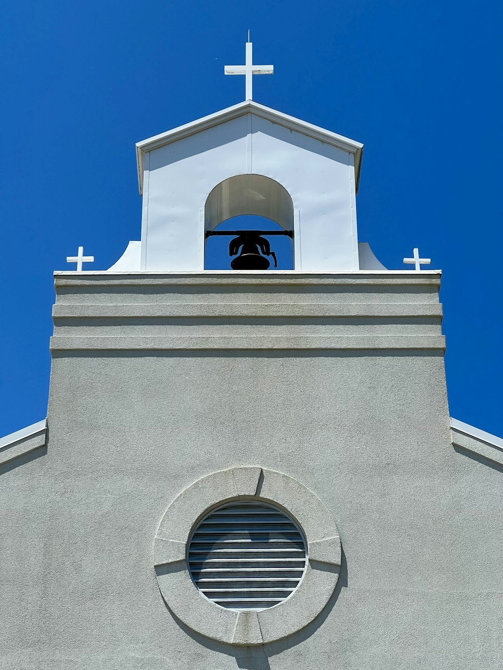 Un edificio blanco con una campana y una cruz en la parte superior