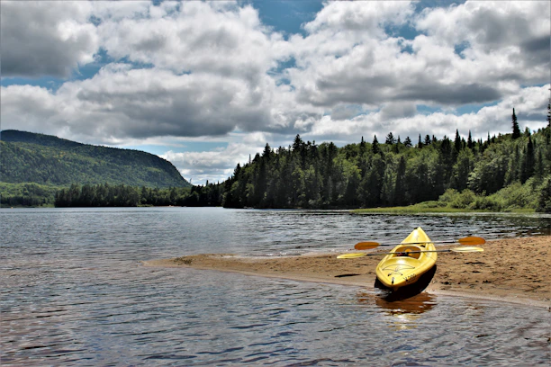 A bright kayak resting on the sandy shore with gentle waves lapping nearby at sunrise.