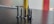 A close-up view of several black screws standing upright on a dark surface, with a blurred background featuring vertical bands of red and yellow.