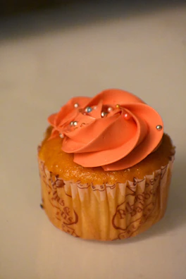A vibrant cupcake topped with swirls of pink frosting and sprinkles.