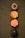 Four cupcakes are neatly arranged in a vertical line on a textured green surface. Each cupcake has distinct frosting designs and colors. The top cupcake has chocolate frosting with a central glossy decoration, resembling a flower or sun. The second cupcake features orange and yellow star-like icing patterns. The third cupcake displays a swirl of pink frosting adorned with small colorful sprinkles. The bottom cupcake has a richly dark chocolate frosting with a glossy finish.